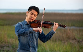 Tianyu Liu plays the violin with the marsh in the background