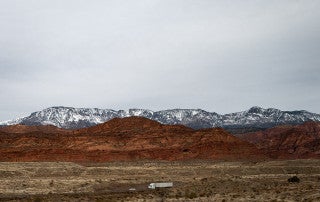 A tractor trailer truck drives on I-95 with mountains in the background in Utah