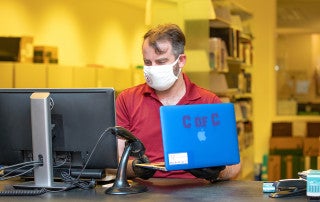 Will Breard checks out a laptop at the Addlestone library circulation desk for a student during the COVID-19 pandemic.