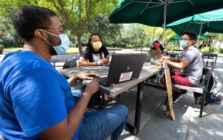 students wearing masks sit at tables outside addlestone library