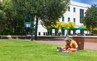 a student sits on the grass outside addlestone library looking at a laptop