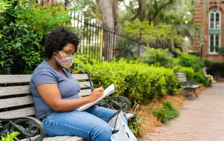 a student takes notes on a park bench outside
