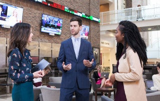 students in the atrium of the beatty center with stock ticker in the background