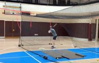 student in a batting cage in silcox gym
