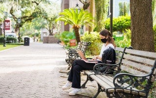 student studies on a bench on cofc campus