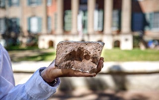 a hand holds a brick with fingerprints in front of randolph hall at the college of charleston