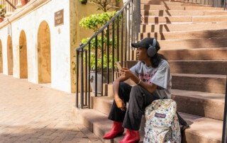 student sits on steps listening to music on headphones