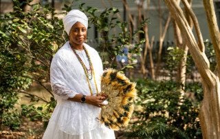 kameelah martin dressed in white holding an ornate feather fan