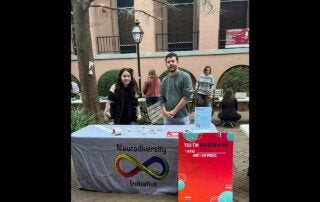 students stand at a table with a neurodiversity initiative sign