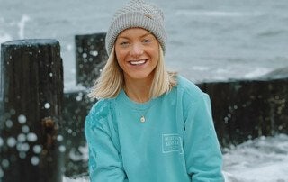 a blond haired woman wearing a teal shirt in front of the ocean