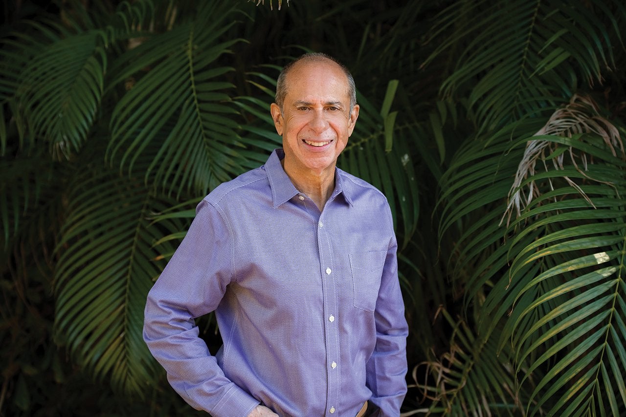 a man wearing a blue shirt stands in front of palm fronds
