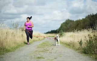 woman running with a dog on a dirt path