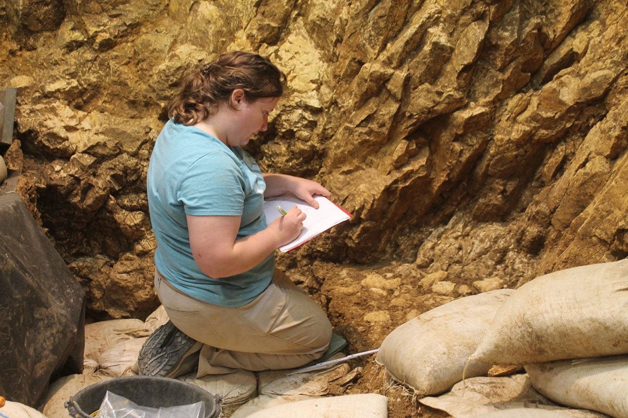 woman kneeling and taking notes at Hohle Fels excavations